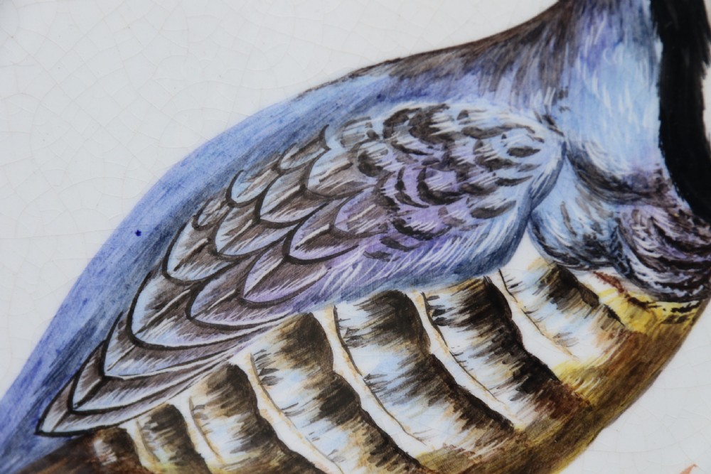 A circular tin-glazed earthenware wall charger featuring a hand-painted game bird in the centre surrounded by a scalloped, floral-decorated rim with blue edging. View XV