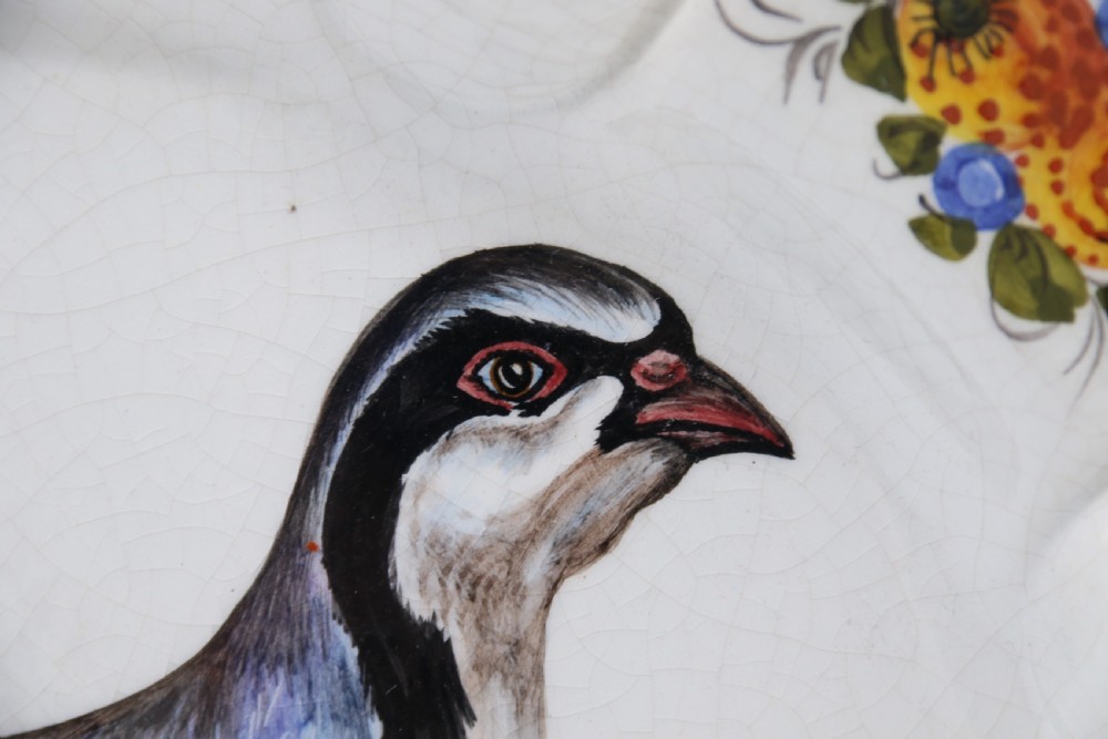 A circular tin-glazed earthenware wall charger featuring a hand-painted game bird in the centre surrounded by a scalloped, floral-decorated rim with blue edging. View XVII