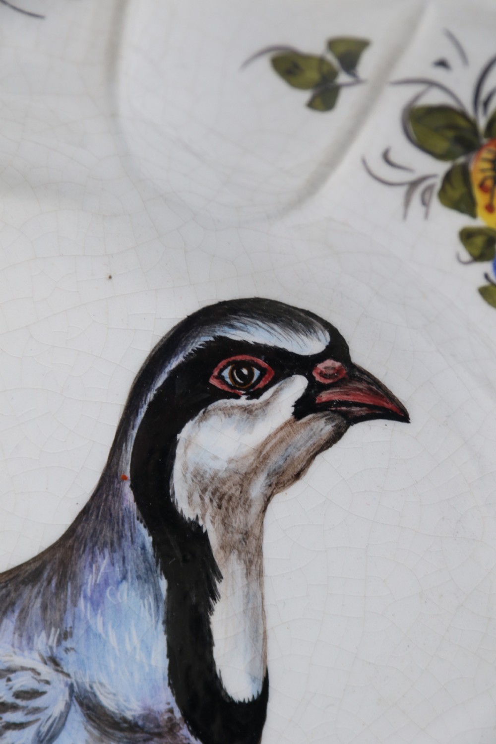 A circular tin-glazed earthenware wall charger featuring a hand-painted game bird in the centre surrounded by a scalloped, floral-decorated rim with blue edging. View XVIII