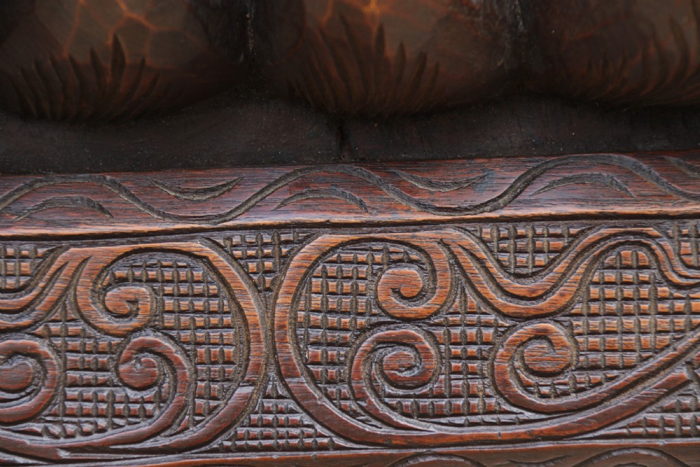 A dark hardwood rectangular panel featuring high-relief carvings of figures riding bullocks and a cart within an ornate carved border. View V