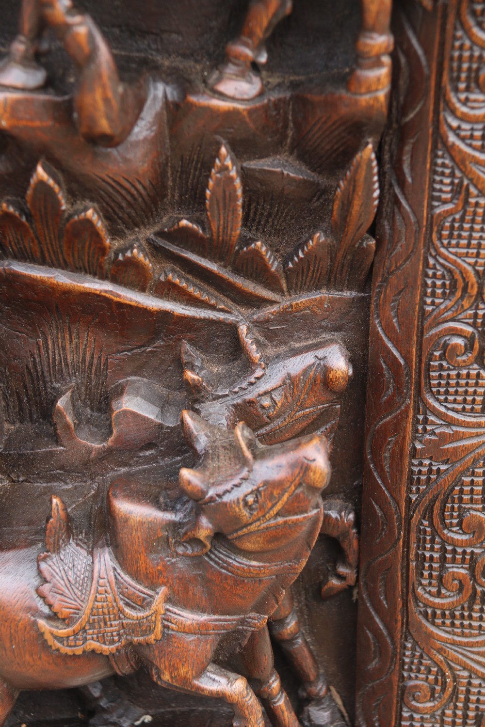 A dark hardwood rectangular panel featuring high-relief carvings of figures riding bullocks and a cart within an ornate carved border. View IX