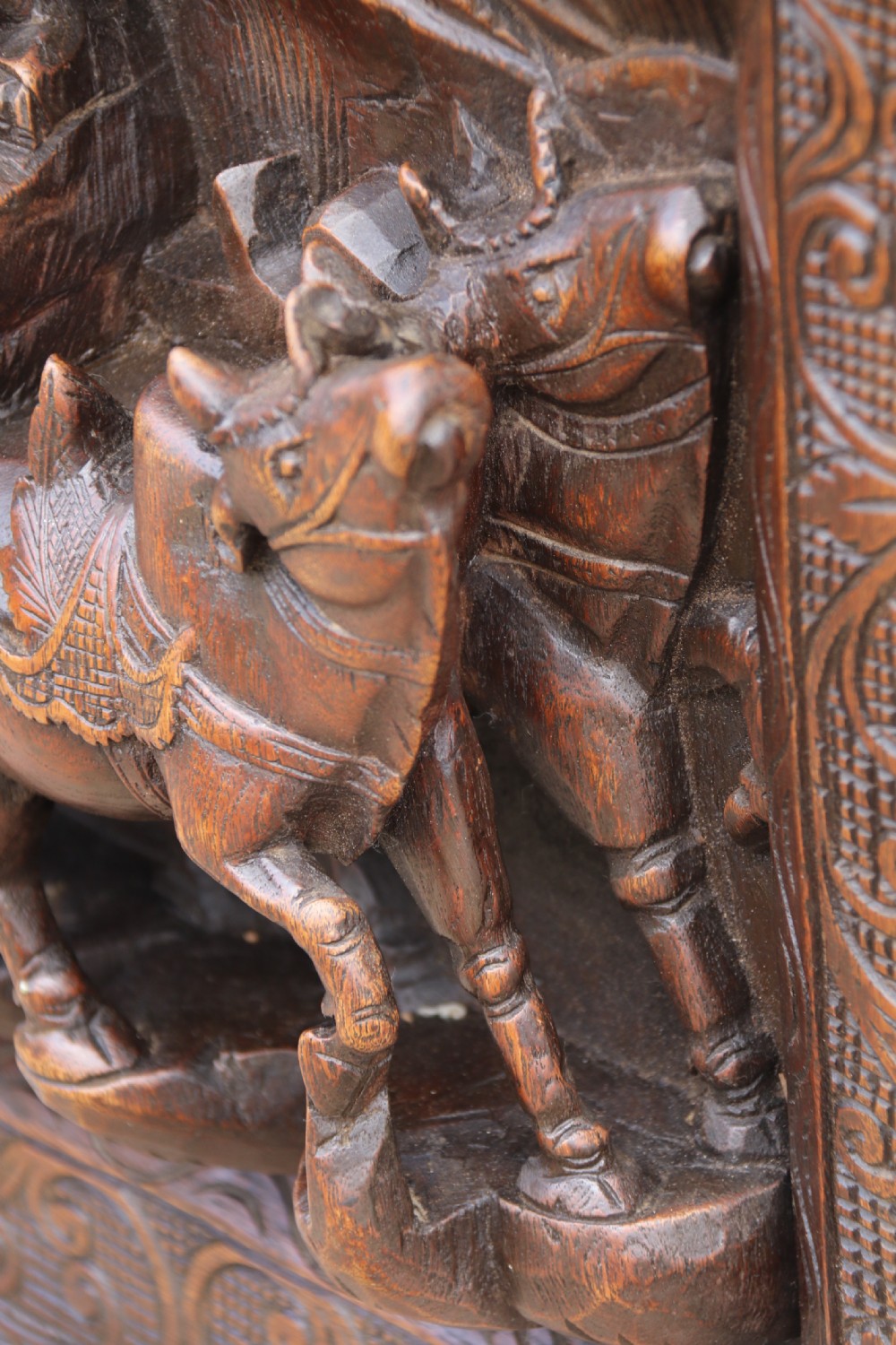 A dark hardwood rectangular panel featuring high-relief carvings of figures riding bullocks and a cart within an ornate carved border. View XI
