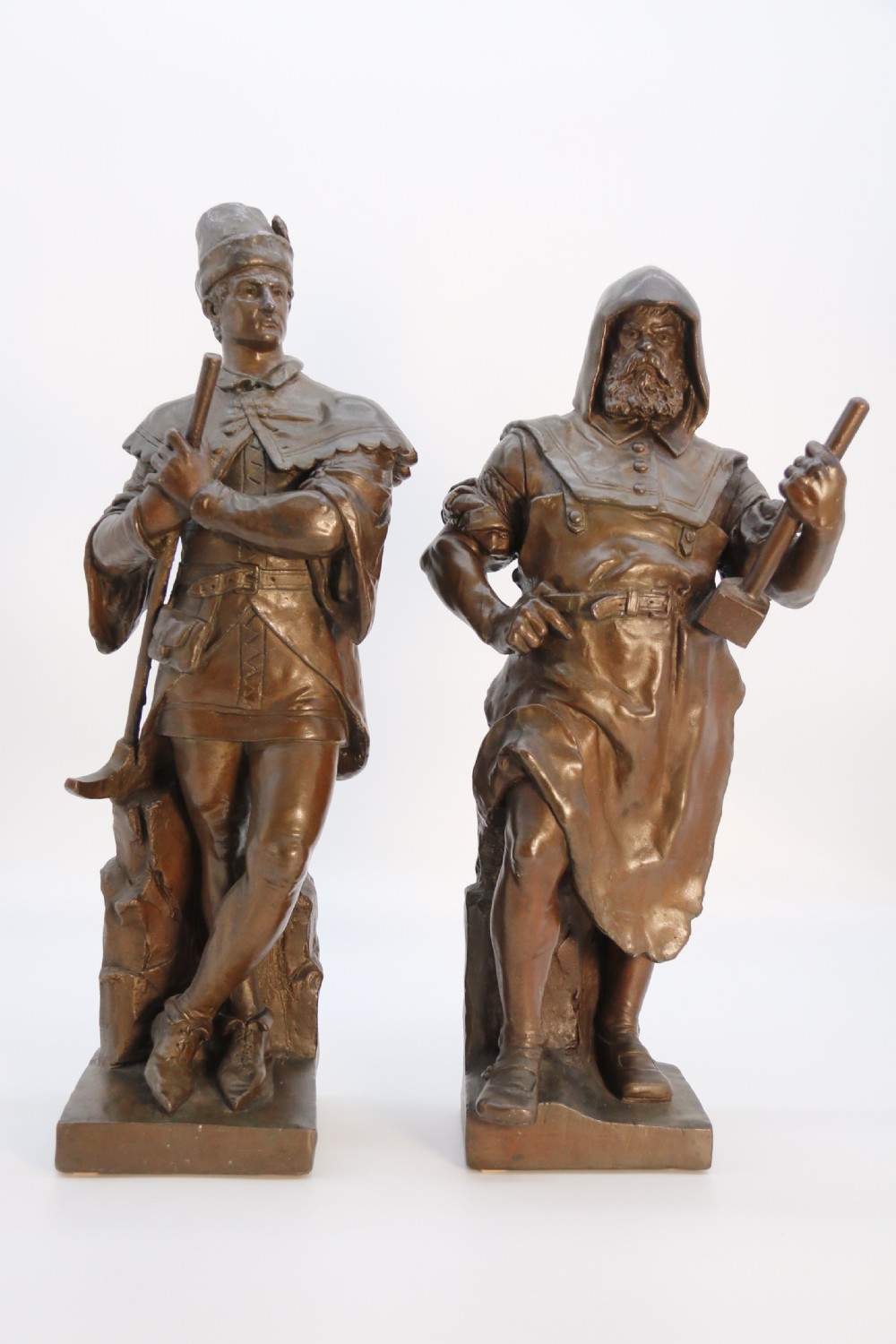 A pair of patinated electrotype bronze figures depicting historic tradesmen standing on rectangular plinths.