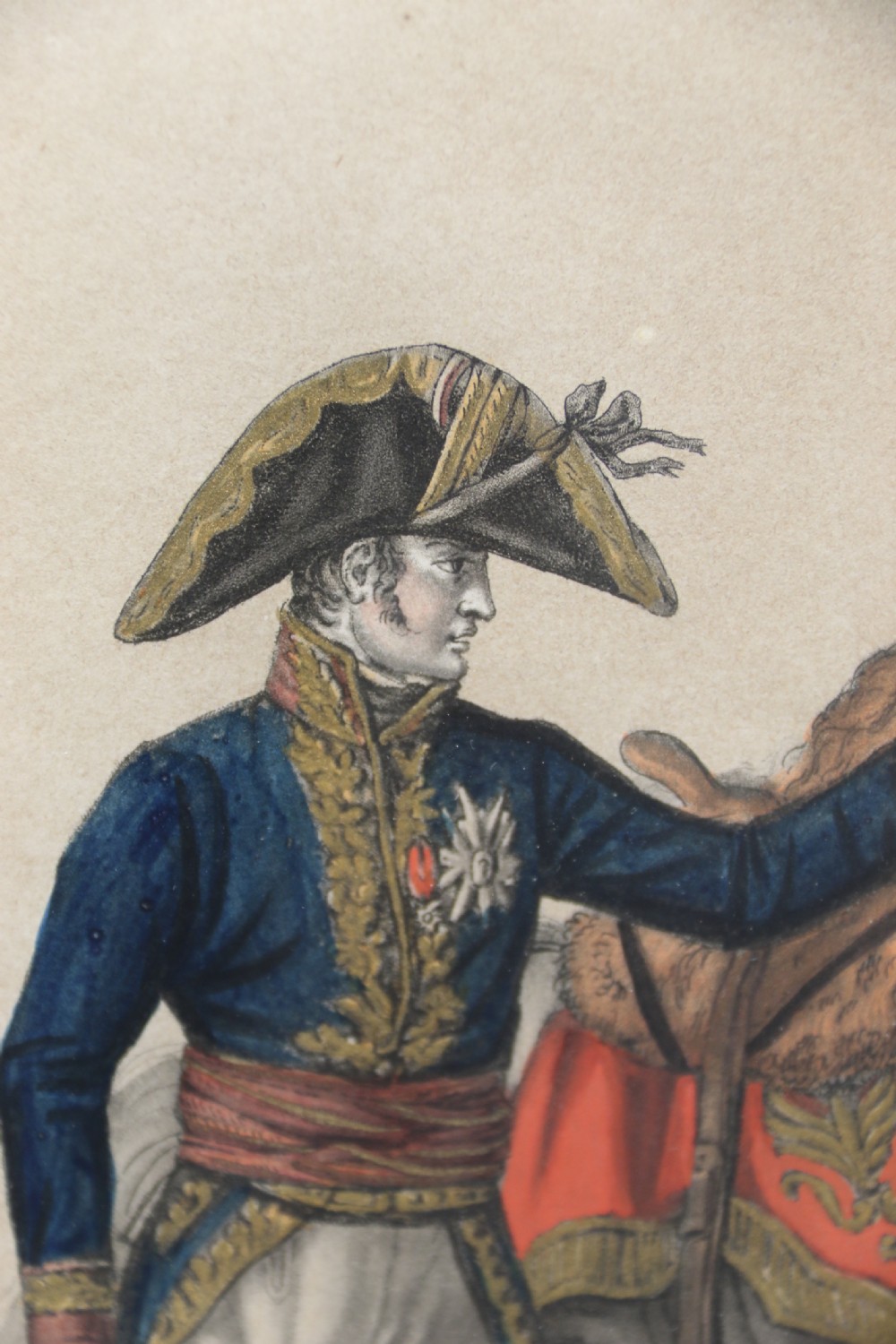 A framed early nineteenth-century hand-coloured print depicting a French Napoleonic military officer standing beside a grey horse in a landscape. View VII