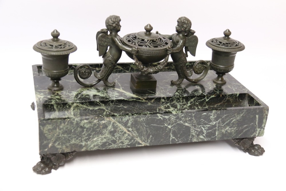 An Empire period dark green marble inkstand featuring dark patinated bronze cherub figures, twin urn inkwells, and carved claw feet. View II