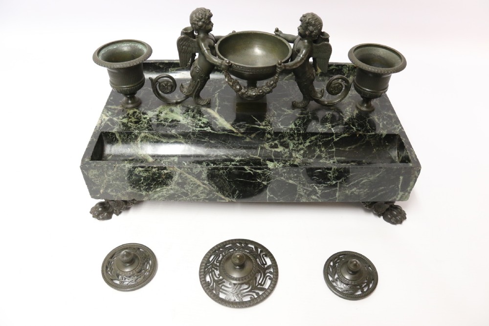 An Empire period dark green marble inkstand featuring dark patinated bronze cherub figures, twin urn inkwells, and carved claw feet. View VI