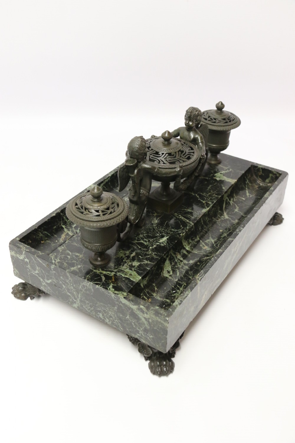 An Empire period dark green marble inkstand featuring dark patinated bronze cherub figures, twin urn inkwells, and carved claw feet. View IX