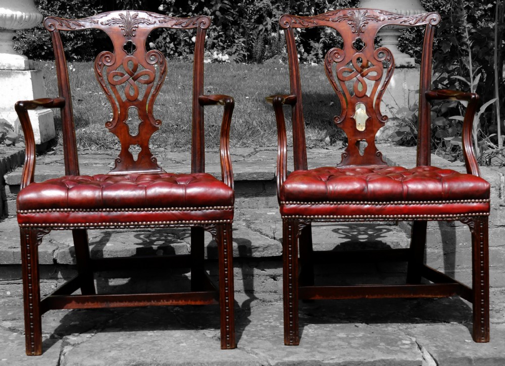 A pair of 18th-century George III Chippendale period mahogany armchairs featuring pierced carved back splats and deep red buttoned leather seats with brass stud trim.