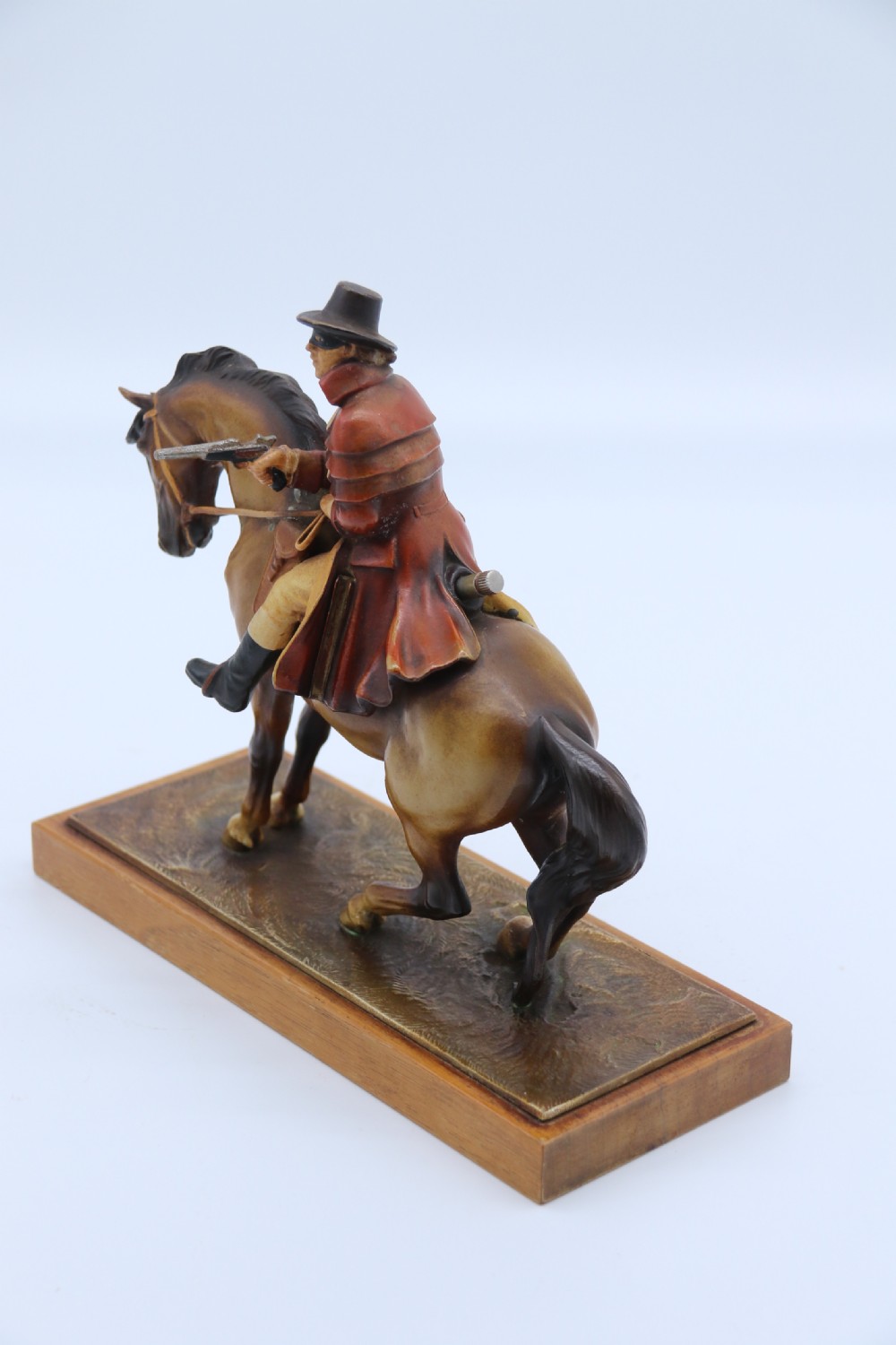 An Art Deco cold-painted metal figure of a masked highwayman on horseback mounted on a rectangular wooden plinth, featuring an integrated table lighter mechanism. View II