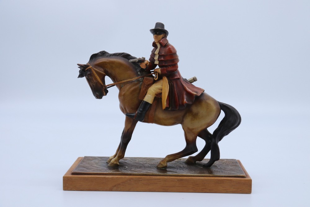 An Art Deco cold-painted metal figure of a masked highwayman on horseback mounted on a rectangular wooden plinth, featuring an integrated table lighter mechanism. View V