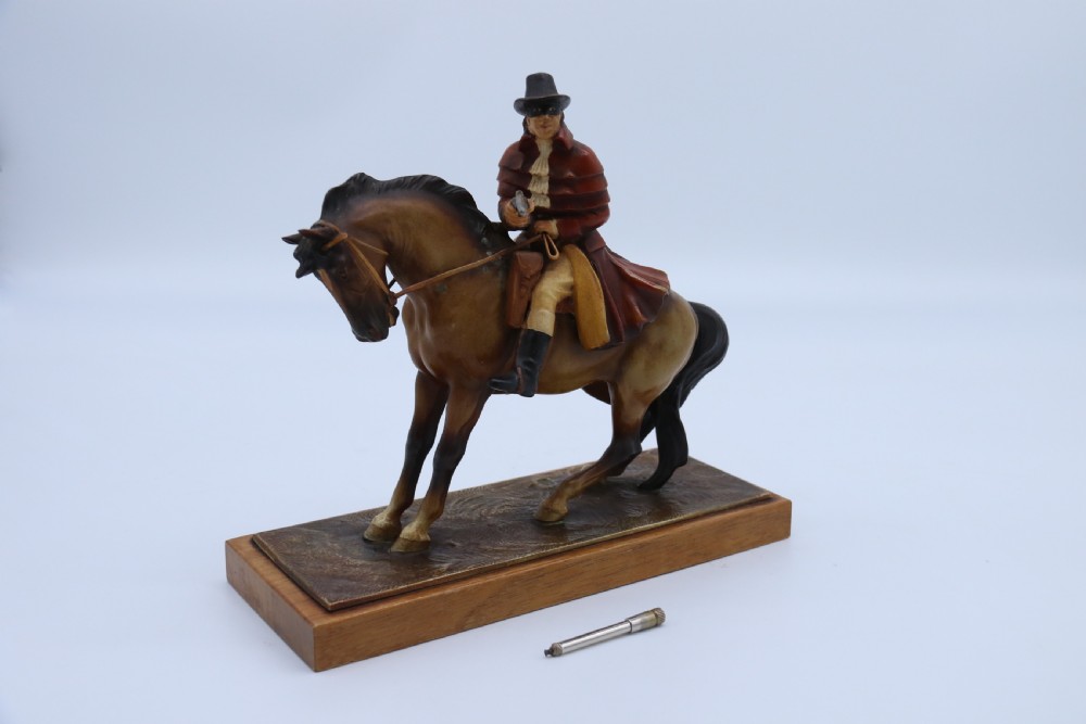 An Art Deco cold-painted metal figure of a masked highwayman on horseback mounted on a rectangular wooden plinth, featuring an integrated table lighter mechanism. View VII
