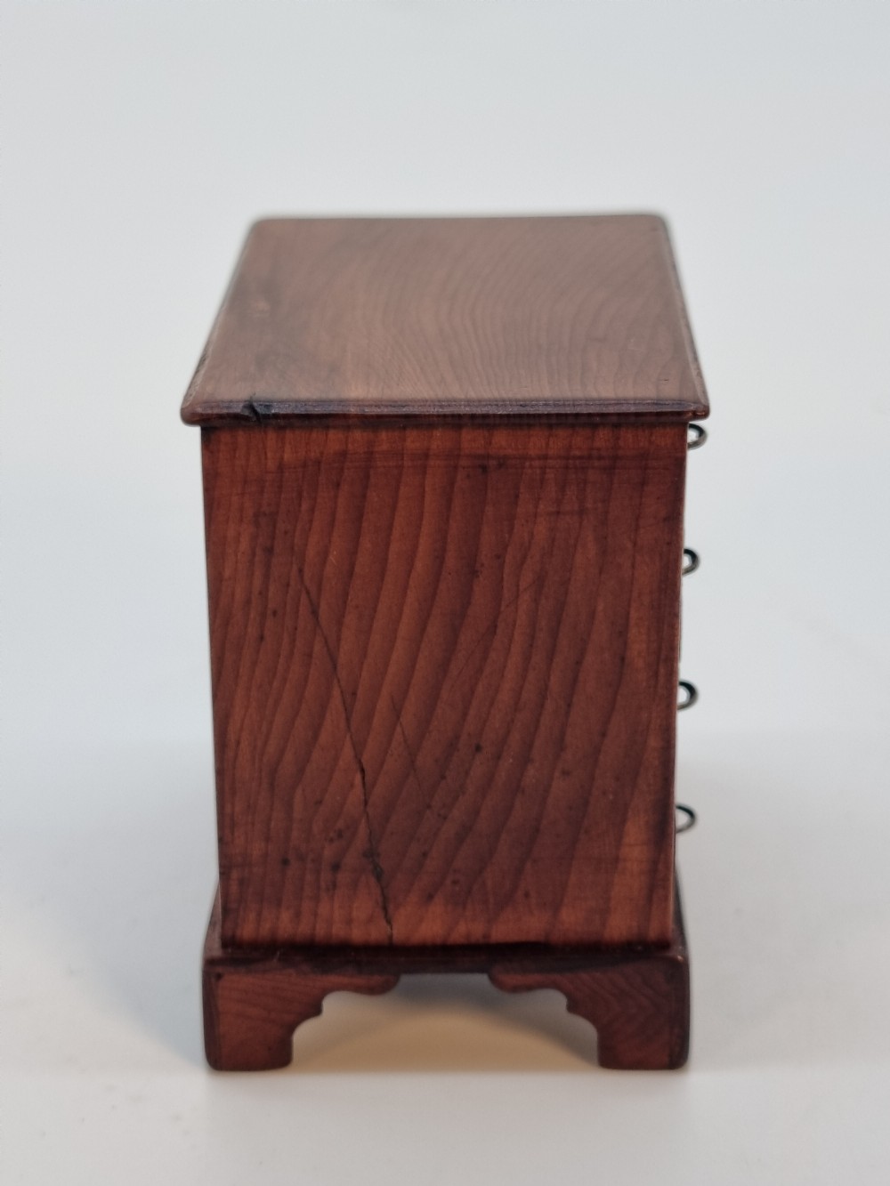 An antique miniature yew wood kneehole desk featuring small drawers, brass handles, and a central cupboard door. View II