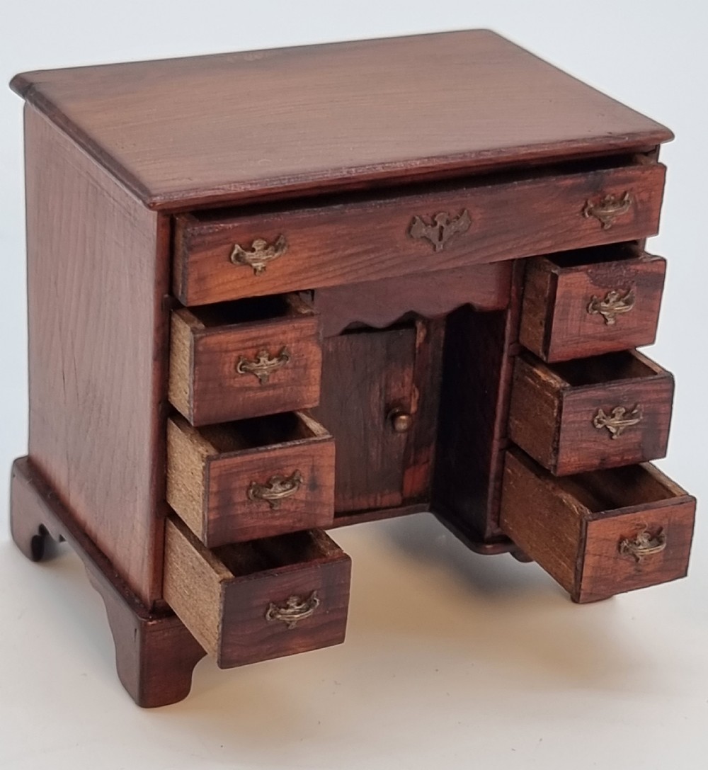 An antique miniature yew wood kneehole desk featuring small drawers, brass handles, and a central cupboard door. View IV
