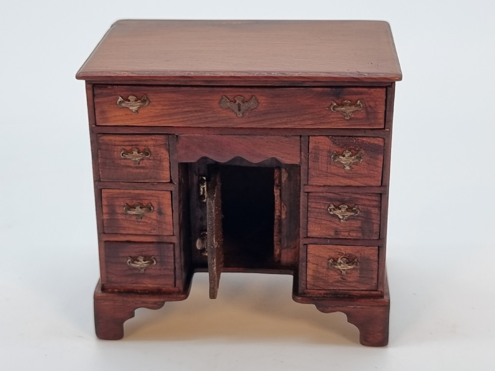 An antique miniature yew wood kneehole desk featuring small drawers, brass handles, and a central cupboard door. View X