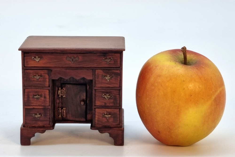 An antique miniature yew wood kneehole desk featuring small drawers, brass handles, and a central cupboard door.