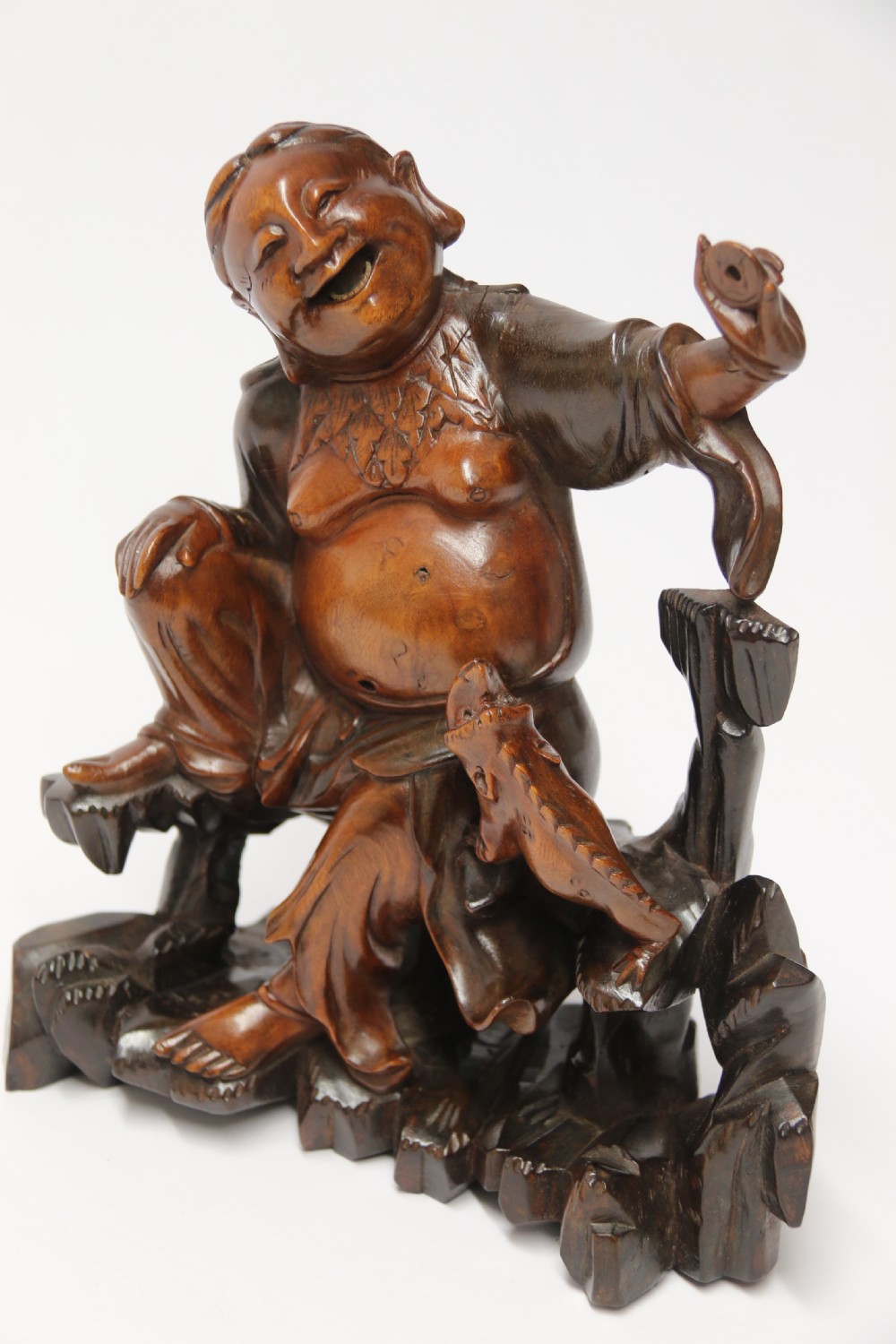 A late nineteenth-century carved brown hardwood figure depicting a seated laughing figure with an open mouth alongside a small mythical creature on a carved rocky base. View III