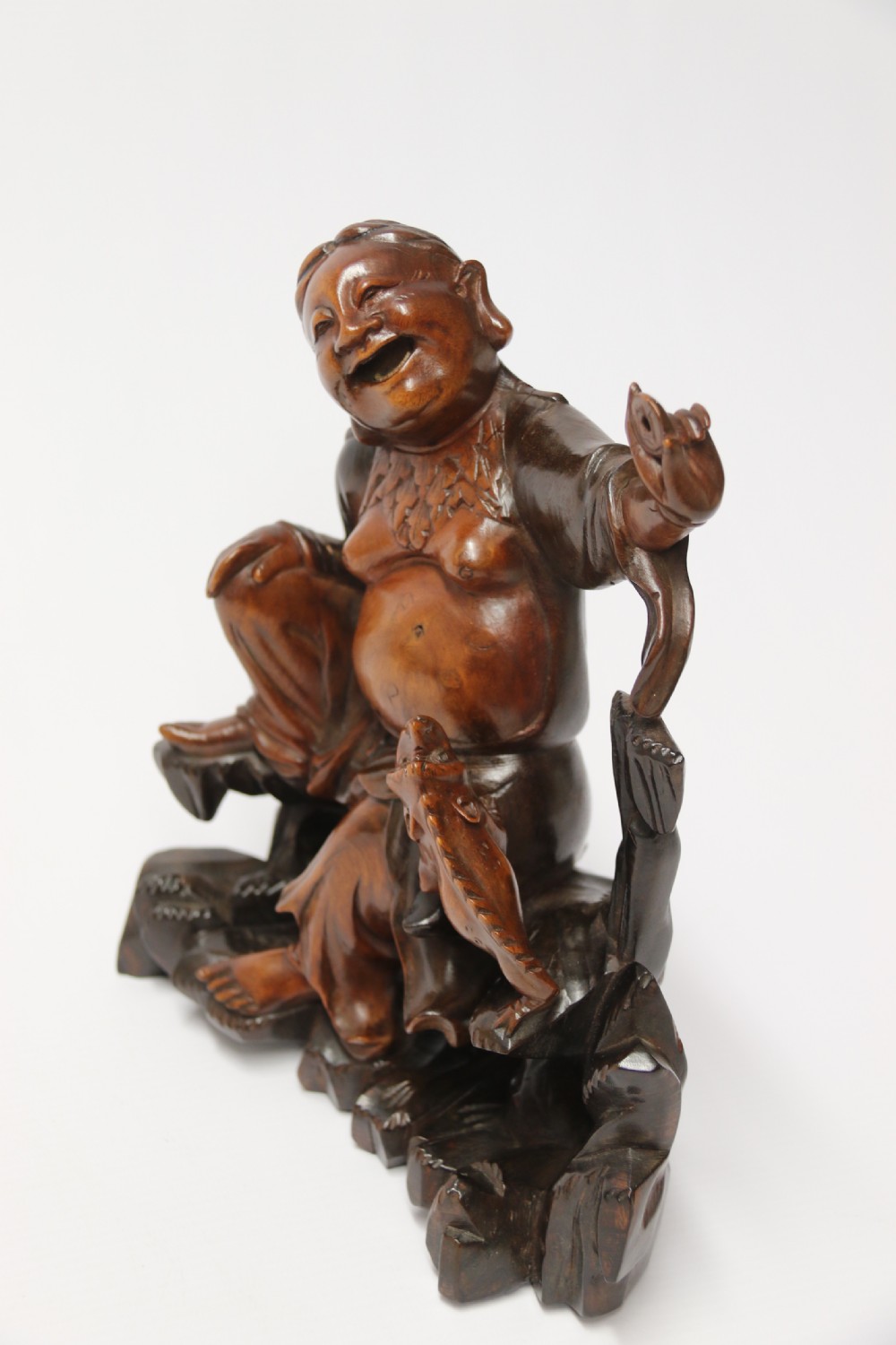 A late nineteenth-century carved brown hardwood figure depicting a seated laughing figure with an open mouth alongside a small mythical creature on a carved rocky base. View IV