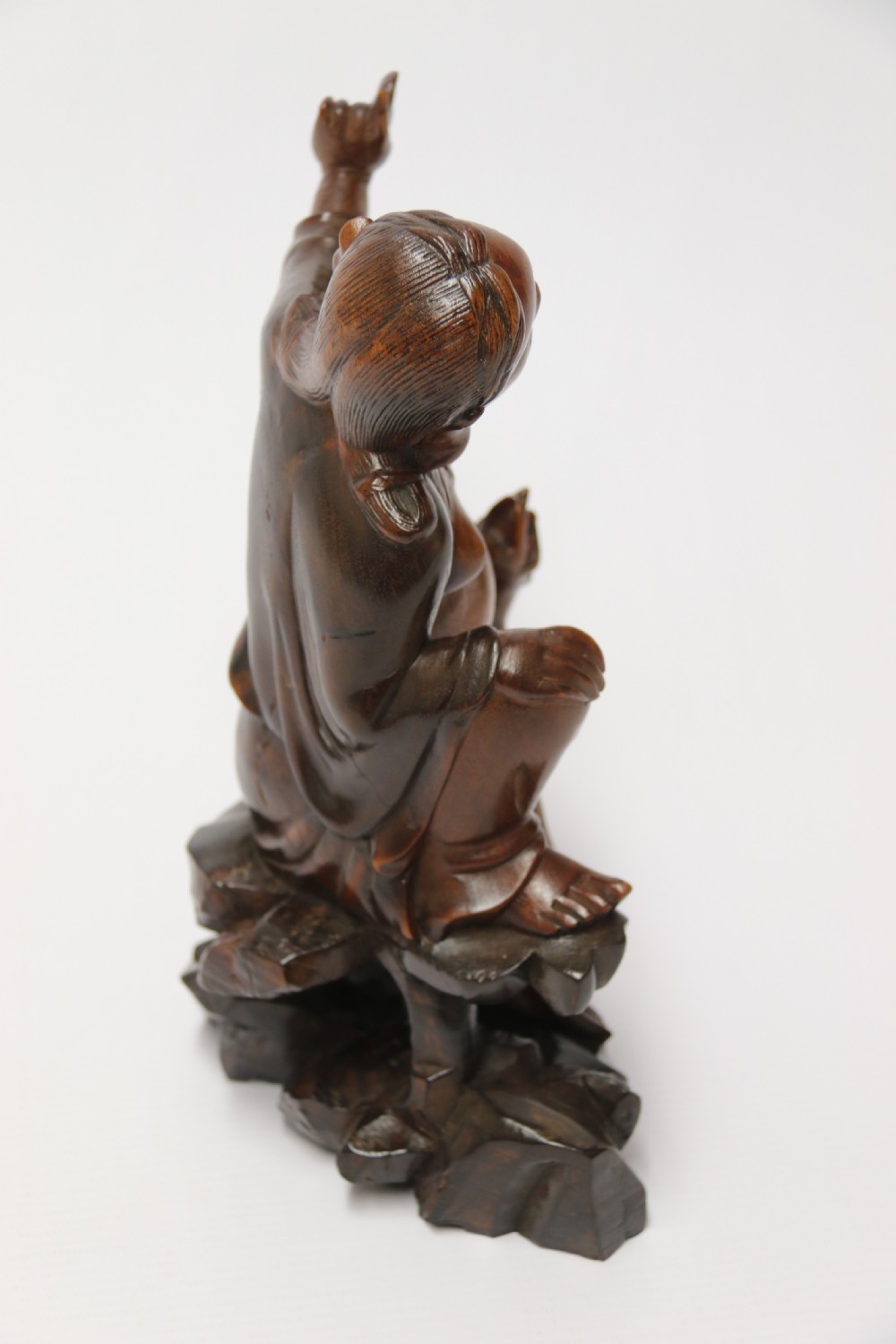 A late nineteenth-century carved brown hardwood figure depicting a seated laughing figure with an open mouth alongside a small mythical creature on a carved rocky base. View IX