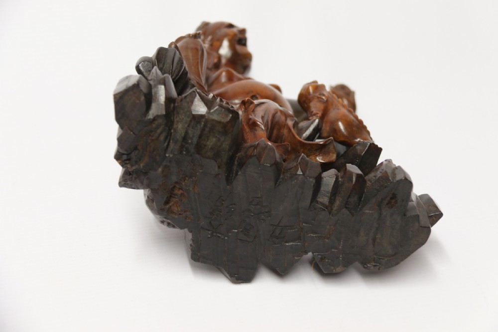 A late nineteenth-century carved brown hardwood figure depicting a seated laughing figure with an open mouth alongside a small mythical creature on a carved rocky base. View XII