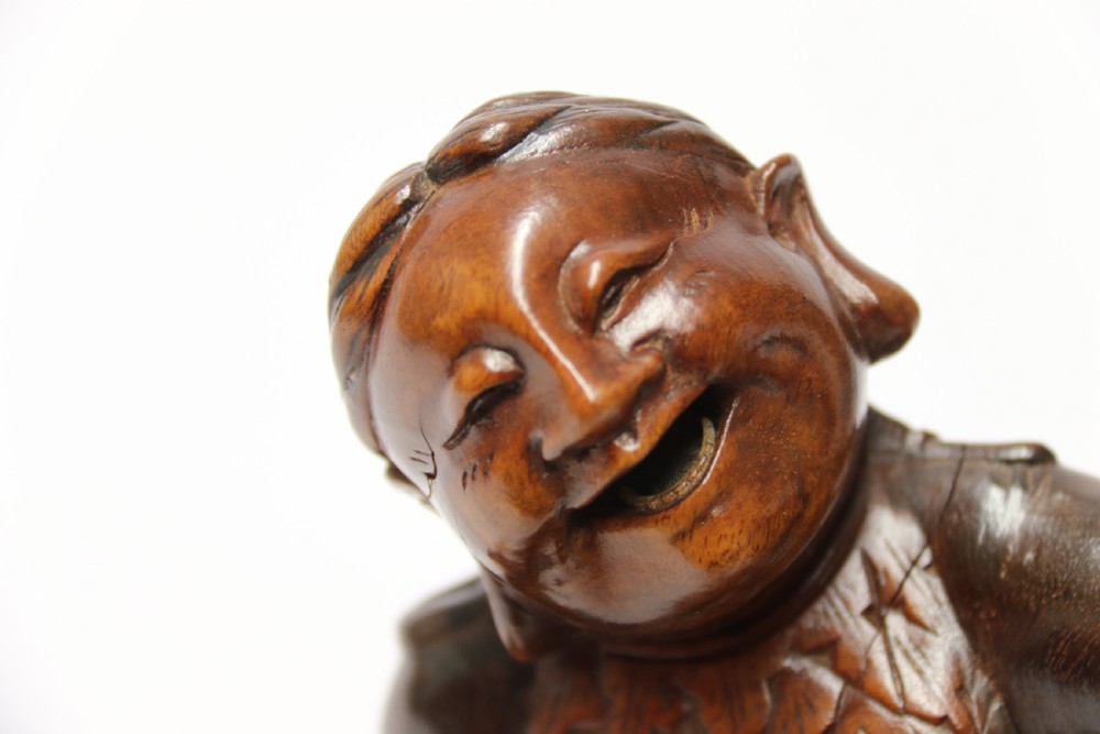 A late nineteenth-century carved brown hardwood figure depicting a seated laughing figure with an open mouth alongside a small mythical creature on a carved rocky base. View XIII