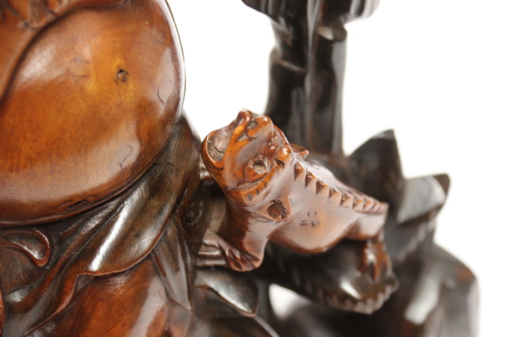 A late nineteenth-century carved brown hardwood figure depicting a seated laughing figure with an open mouth alongside a small mythical creature on a carved rocky base. View XV