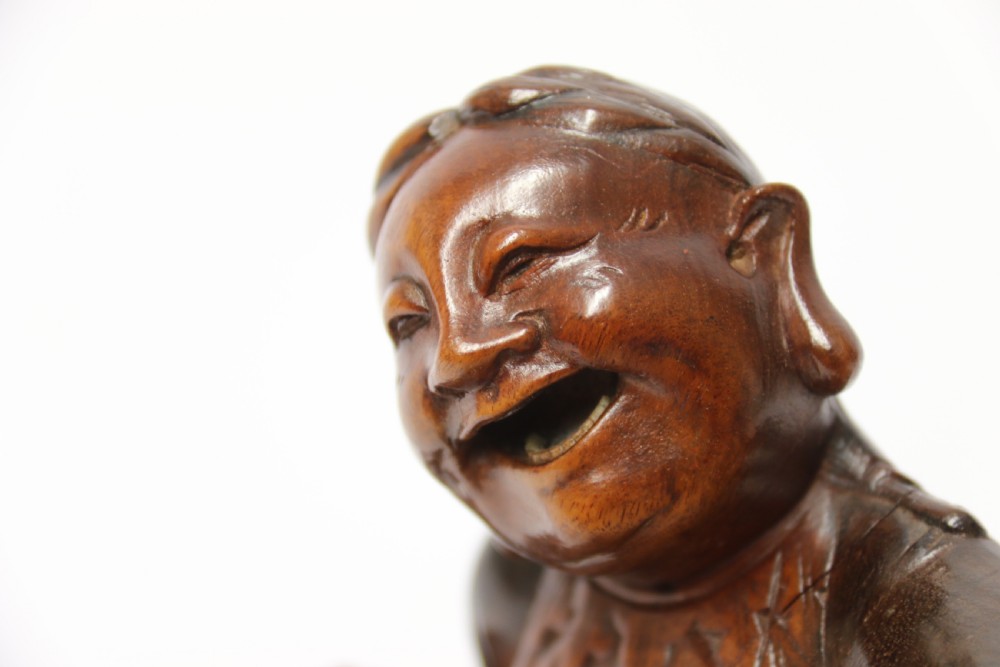 A late nineteenth-century carved brown hardwood figure depicting a seated laughing figure with an open mouth alongside a small mythical creature on a carved rocky base. View XVI