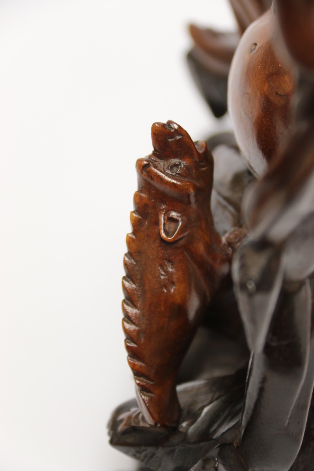 A late nineteenth-century carved brown hardwood figure depicting a seated laughing figure with an open mouth alongside a small mythical creature on a carved rocky base. View XVII