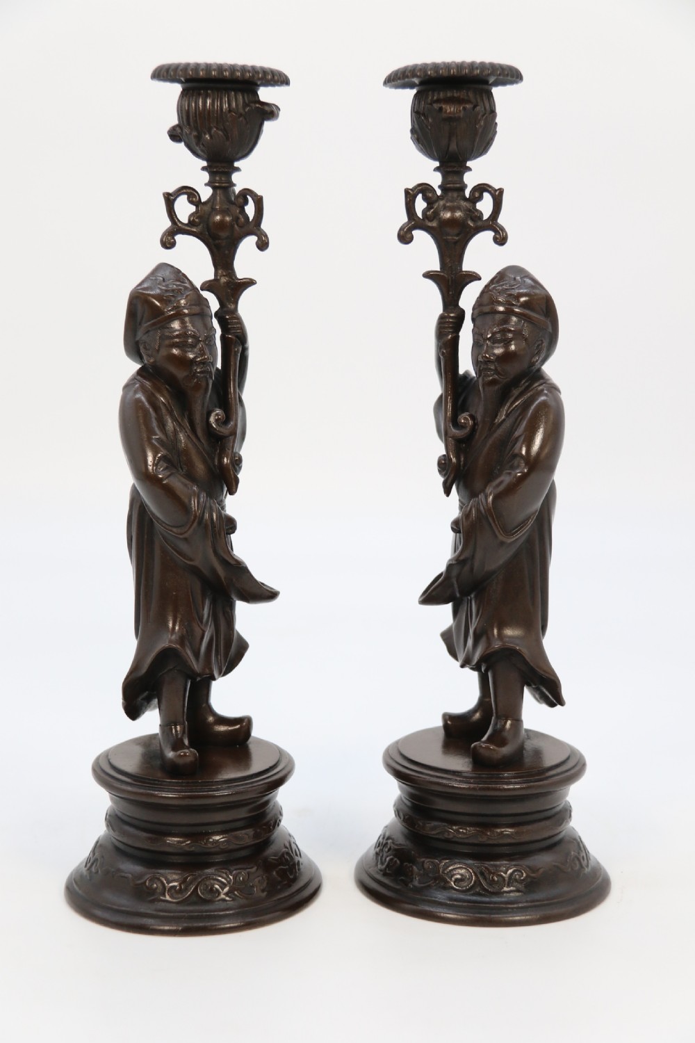 A pair of 19th-century French dark bronze candlesticks sculpted as standing Chinese figures holding flower-shaped candle nozzles on stepped round bases. View XVI