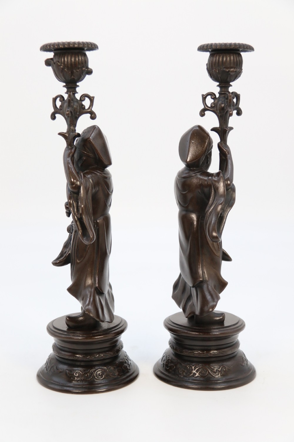 A pair of 19th-century French dark bronze candlesticks sculpted as standing Chinese figures holding flower-shaped candle nozzles on stepped round bases. View XX