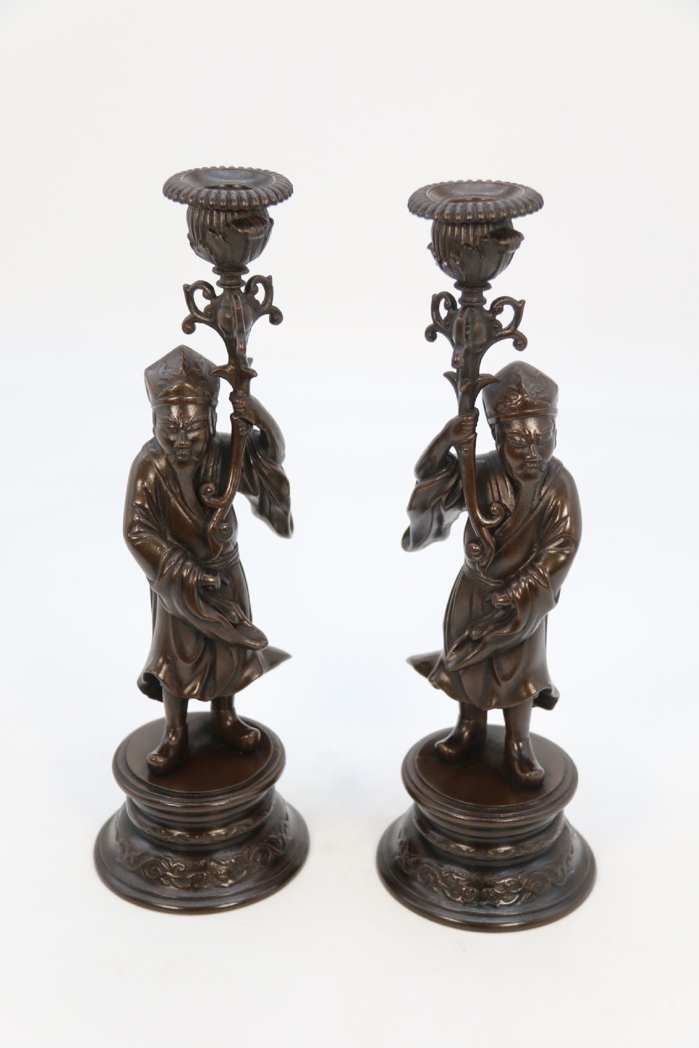 A pair of 19th-century French dark bronze candlesticks sculpted as standing Chinese figures holding flower-shaped candle nozzles on stepped round bases. View XXX