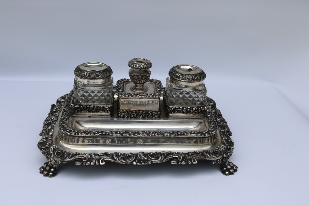 An early nineteenth-century Sheffield plate desk inkstand featuring two cut-glass inkwells and decorative scroll borders raised on paw feet. View II