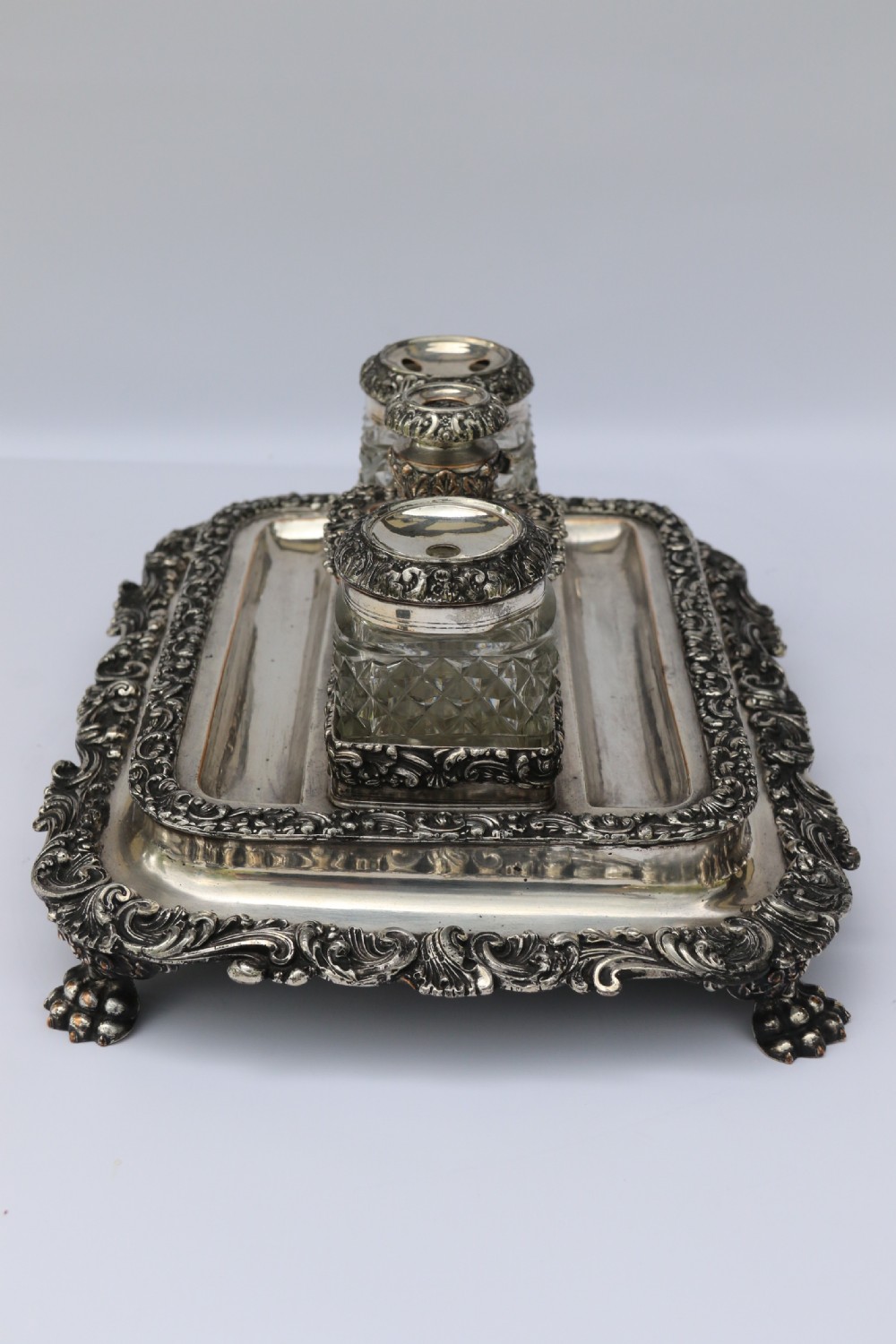 An early nineteenth-century Sheffield plate desk inkstand featuring two cut-glass inkwells and decorative scroll borders raised on paw feet. View VII