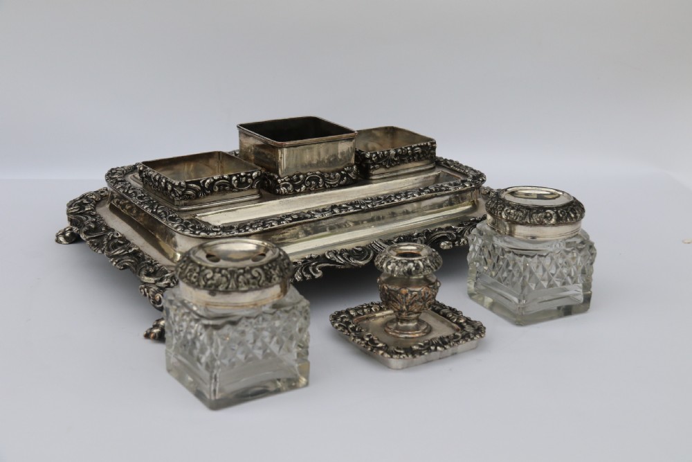 An early nineteenth-century Sheffield plate desk inkstand featuring two cut-glass inkwells and decorative scroll borders raised on paw feet. View X