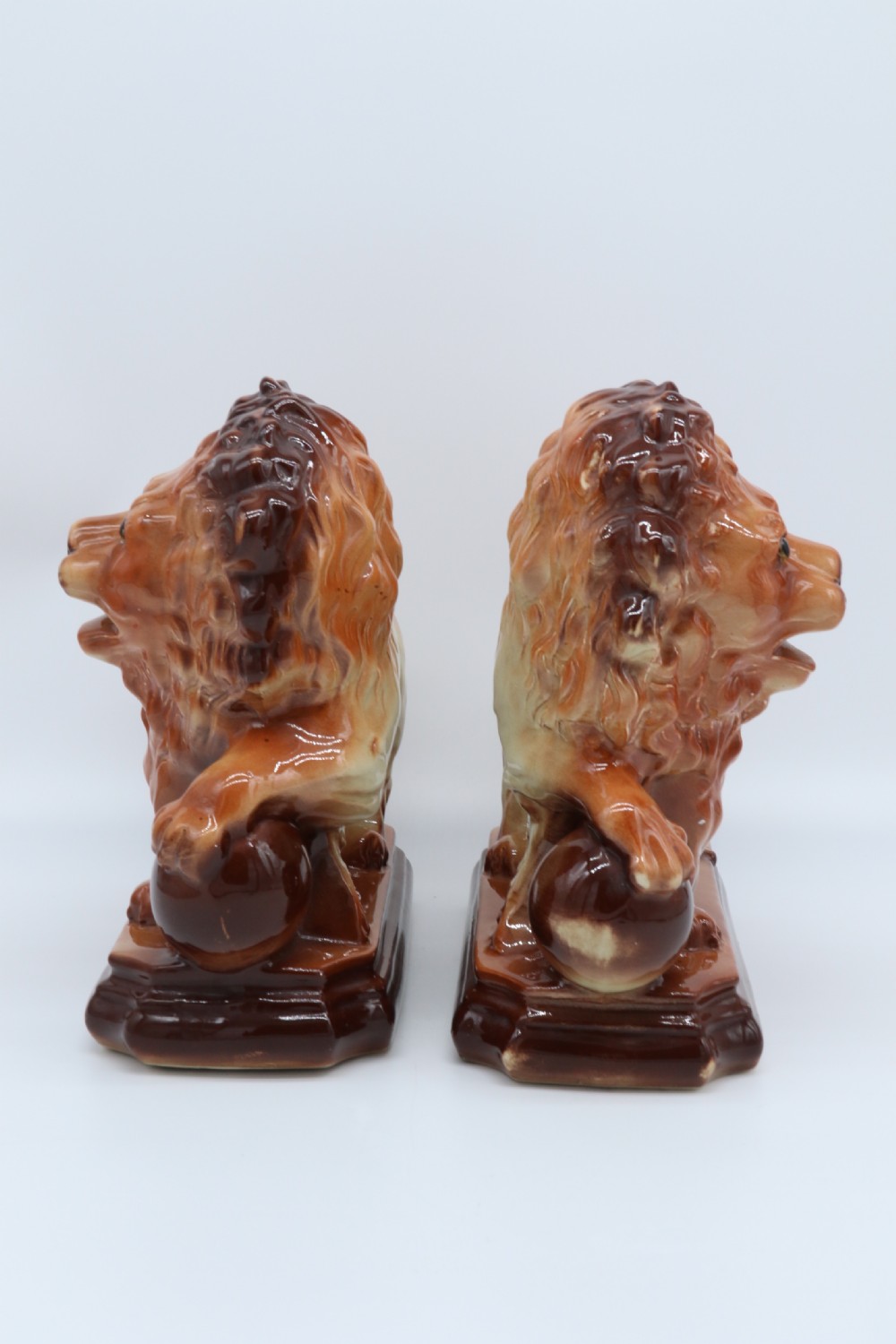A pair of warm brown glazed earthenware Medici lion figurines standing on integral bases with one front paw resting on a ball. View II