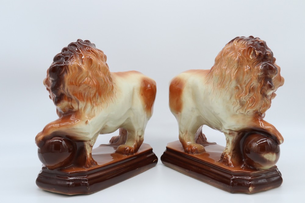 A pair of warm brown glazed earthenware Medici lion figurines standing on integral bases with one front paw resting on a ball. View III
