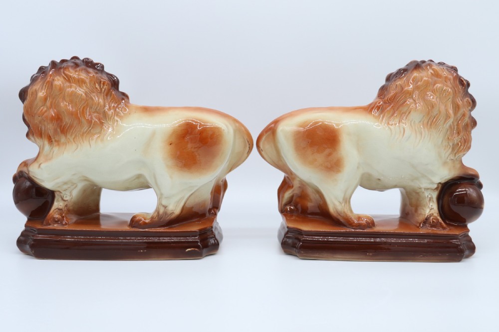 A pair of warm brown glazed earthenware Medici lion figurines standing on integral bases with one front paw resting on a ball. View V