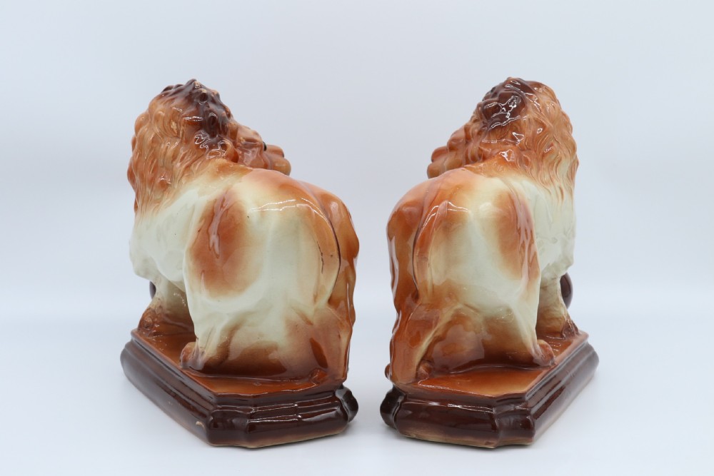 A pair of warm brown glazed earthenware Medici lion figurines standing on integral bases with one front paw resting on a ball. View VI