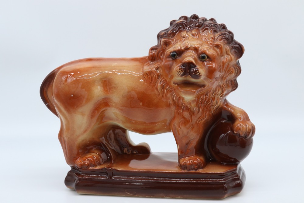 A pair of warm brown glazed earthenware Medici lion figurines standing on integral bases with one front paw resting on a ball. View VII
