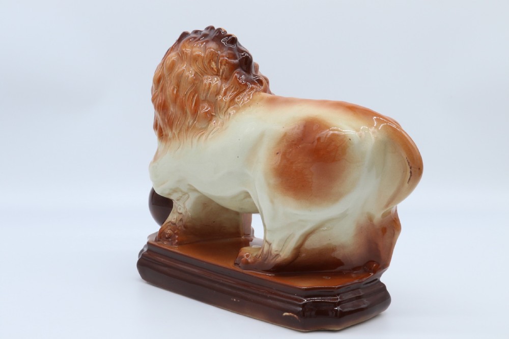 A pair of warm brown glazed earthenware Medici lion figurines standing on integral bases with one front paw resting on a ball. View X