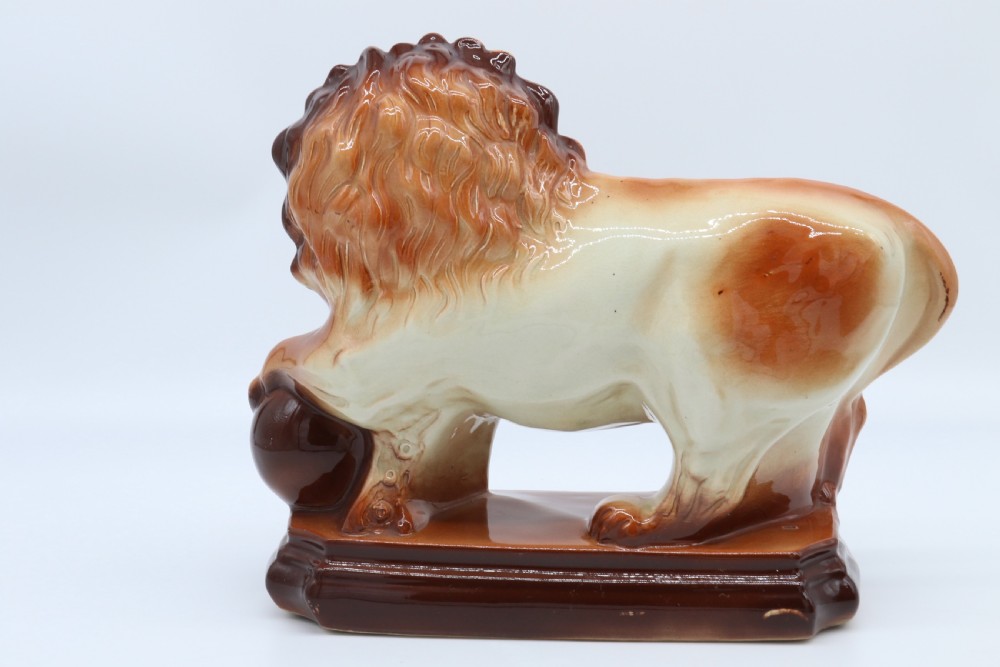 A pair of warm brown glazed earthenware Medici lion figurines standing on integral bases with one front paw resting on a ball. View XI