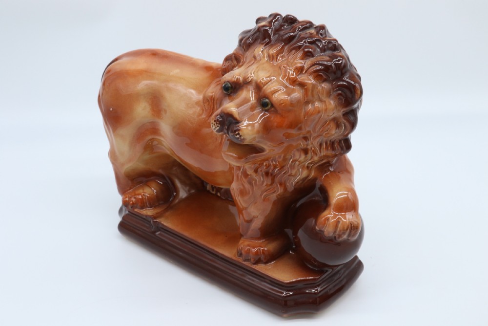 A pair of warm brown glazed earthenware Medici lion figurines standing on integral bases with one front paw resting on a ball. View XII