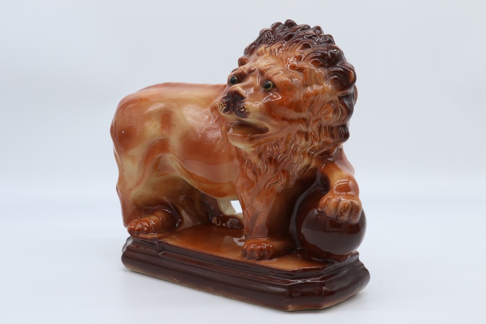 A pair of warm brown glazed earthenware Medici lion figurines standing on integral bases with one front paw resting on a ball. View XV