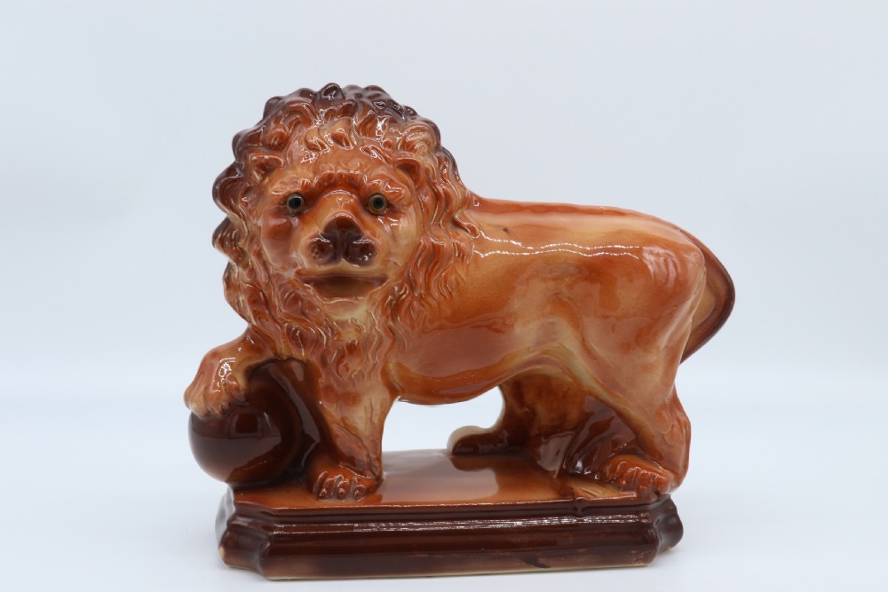 A pair of warm brown glazed earthenware Medici lion figurines standing on integral bases with one front paw resting on a ball. View XVIII