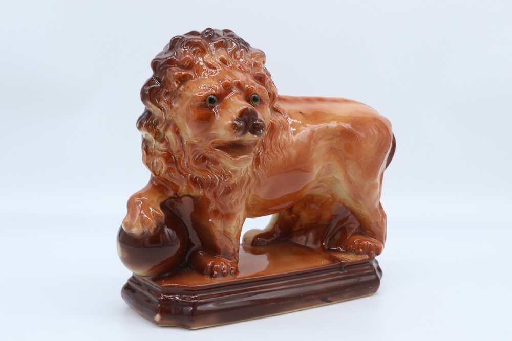A pair of warm brown glazed earthenware Medici lion figurines standing on integral bases with one front paw resting on a ball. View XIX