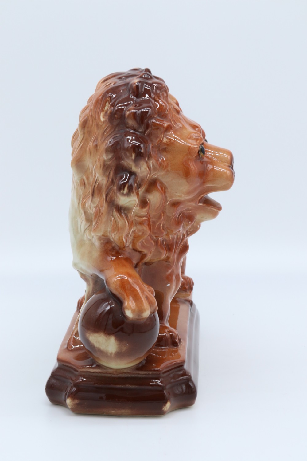 A pair of warm brown glazed earthenware Medici lion figurines standing on integral bases with one front paw resting on a ball. View XX