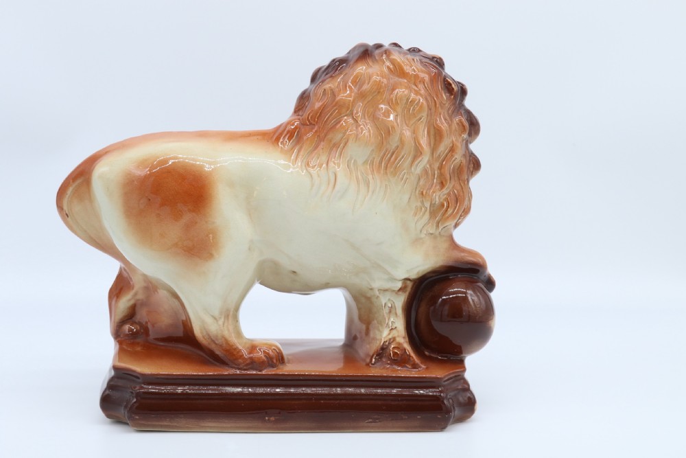 A pair of warm brown glazed earthenware Medici lion figurines standing on integral bases with one front paw resting on a ball. View XXIII