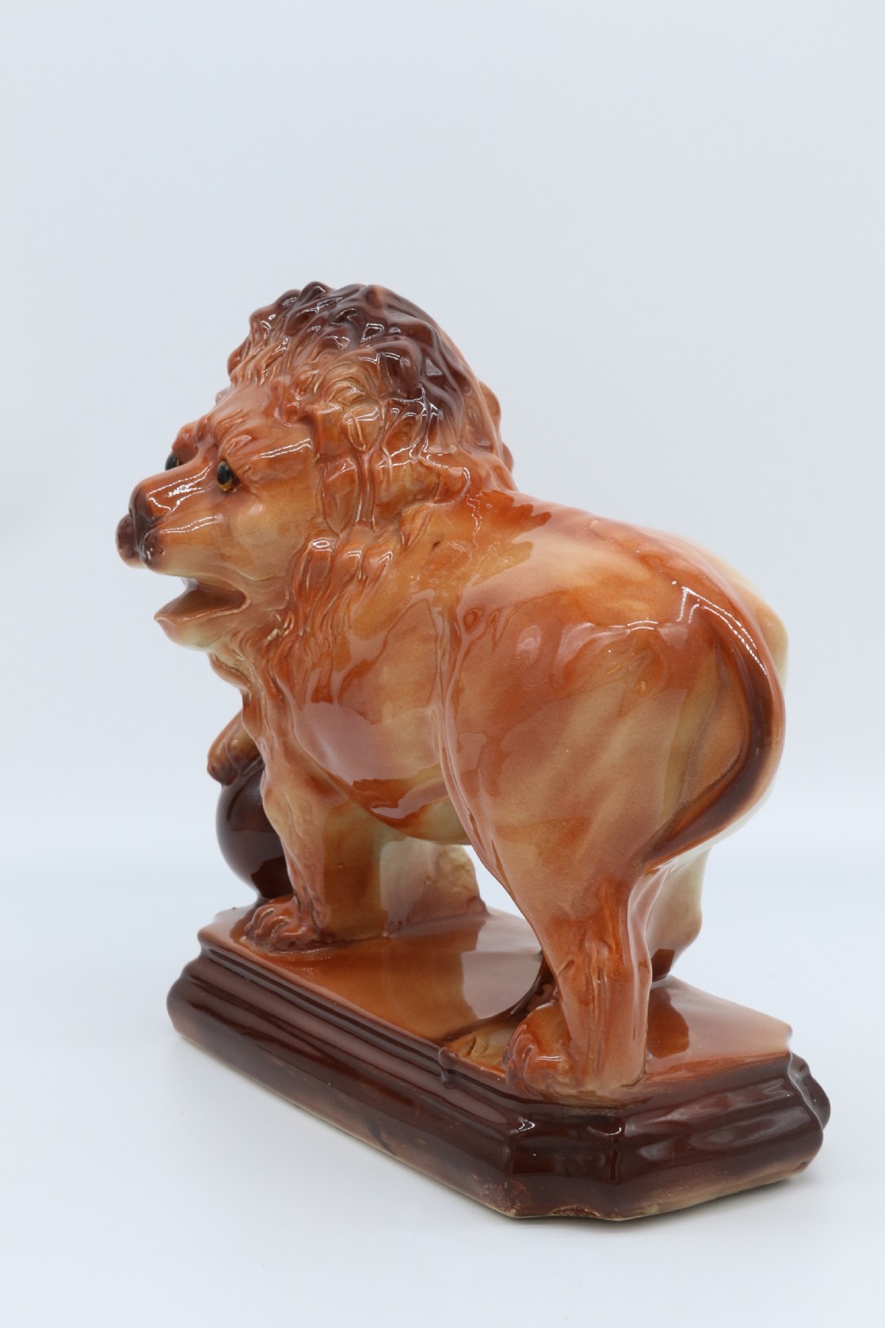 A pair of warm brown glazed earthenware Medici lion figurines standing on integral bases with one front paw resting on a ball. View XXV