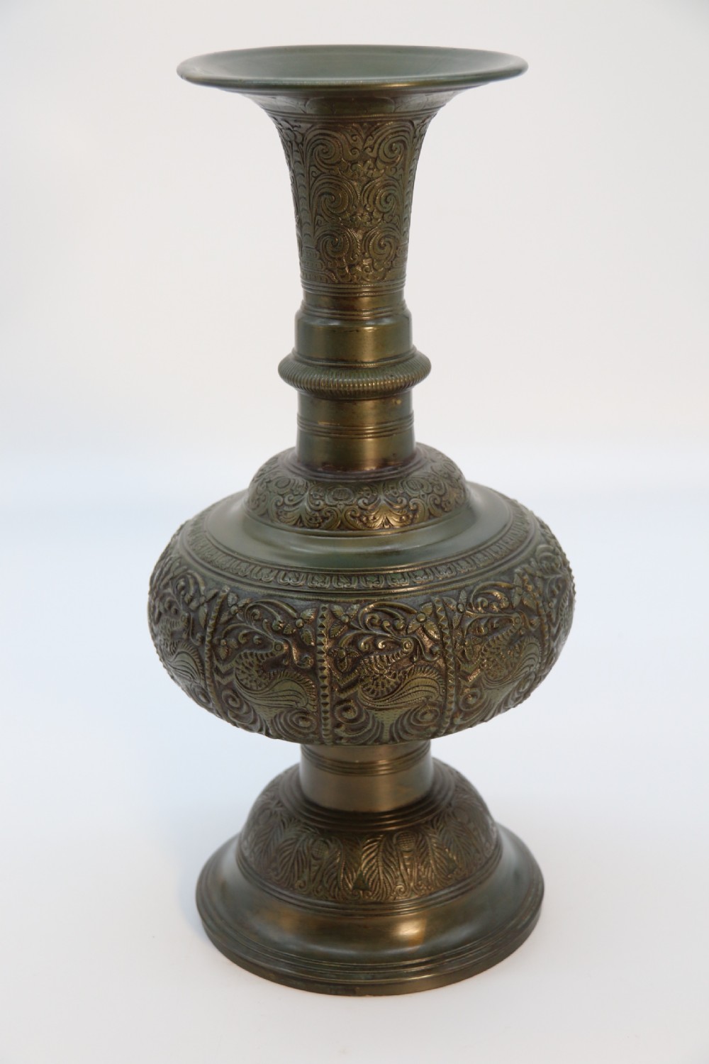 An antique nineteenth-century patinated bronze vase featuring hand-chased floral and foliate motifs, a bulbous center, flared neck, and circular base.