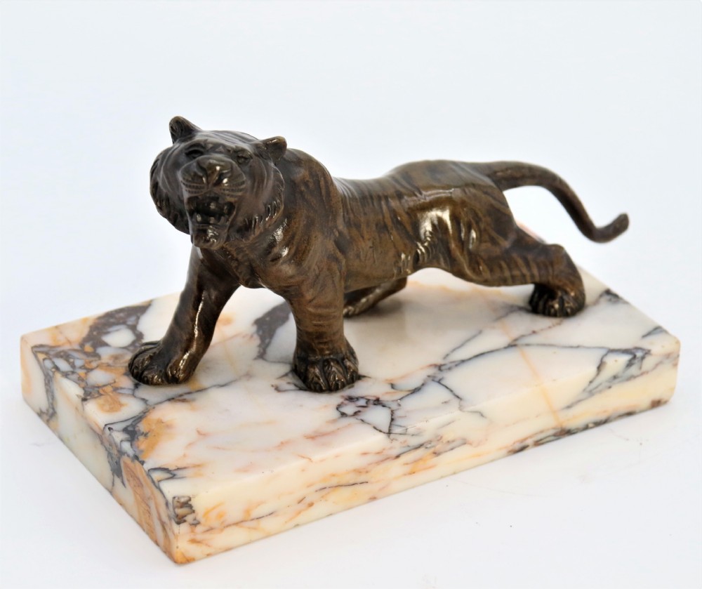 A dark bronze tiger sculpture posed in a roaring stance, mounted on a rectangular veined marble base.