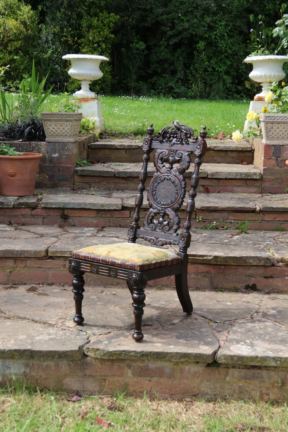 A 19th-century high-backed dark walnut chair featuring intricate floral, bird, and acanthus leaf wood carvings and a patterned upholstered seat. View V